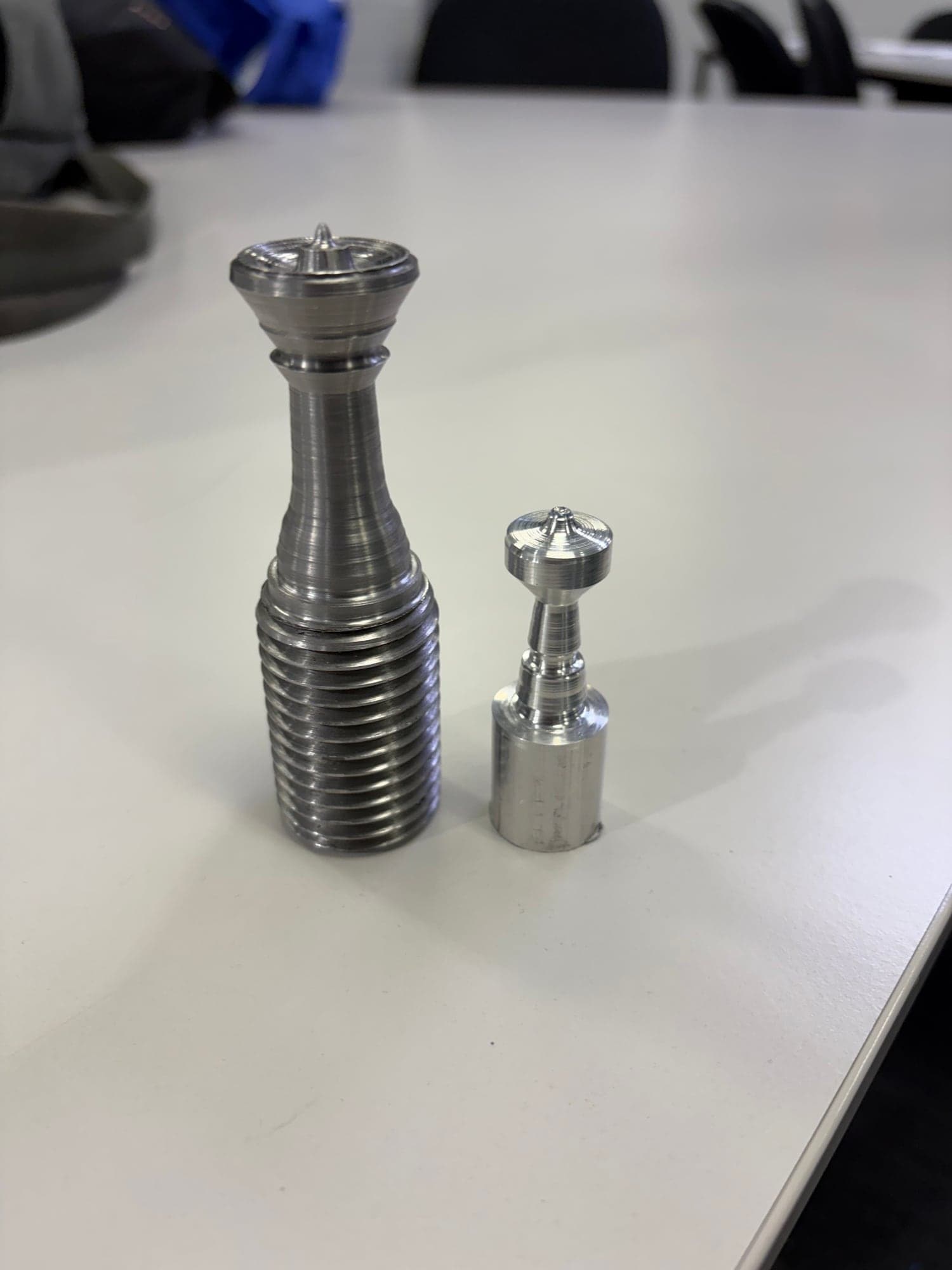 Two aluminium pieces turned on a lathe, one with a threaded base